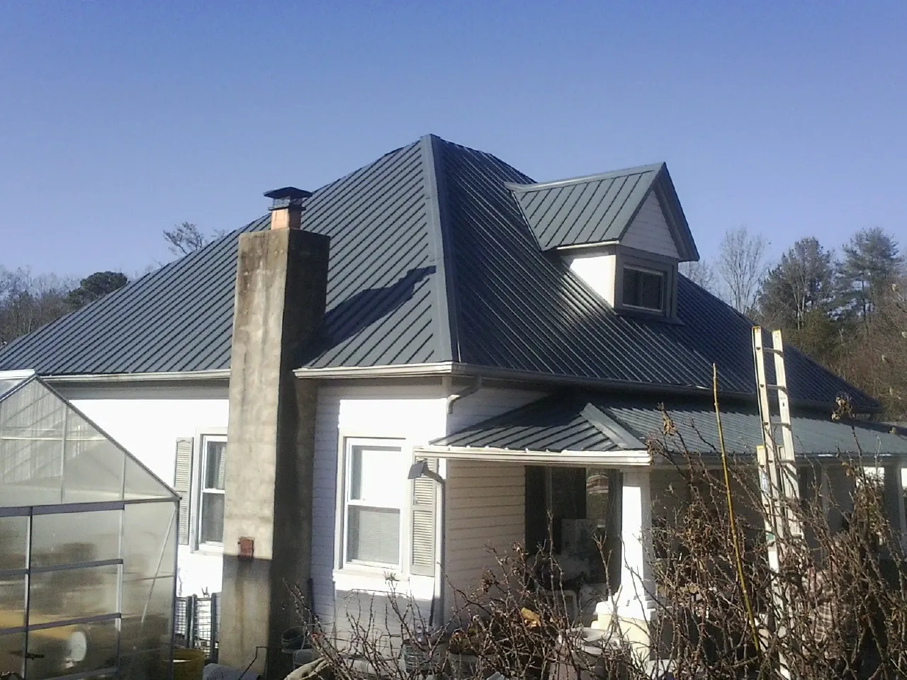 Dark blue standing seam metal roof on a white farmhouse with dormer — Slate & Tile Roof Repair by Roofing Brothers in Bennettsville