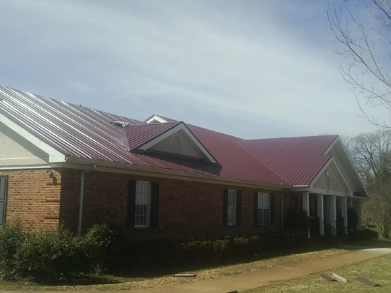 Red metal roof with gabled entries on a long brick building, from a Hail Damage Roof Repair job in Bennettsville