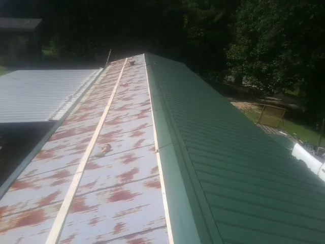 Old rusted panels beside newly installed green metal roofing — Wind Damage Roof Repair by Roofing Brothers in Bennettsville