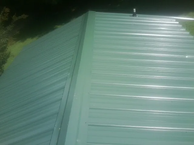New green metal panels meeting at the ridge of a roof — Flat Roof Repair work by our crew in Bennettsville