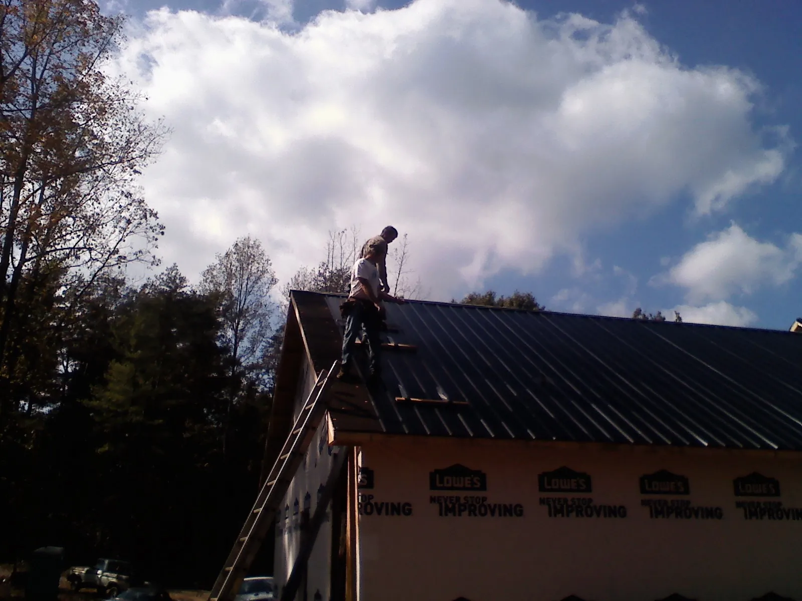 Roofer fastening dark metal panels high against a cloudy sky, from a Roof Inspection job in Bennettsville