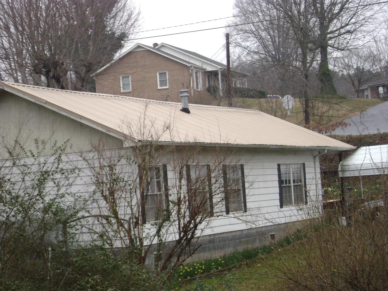 Tan metal roof on a white sided house set into a hillside — Commercial Roofing by Roofing Brothers in Bennettsville